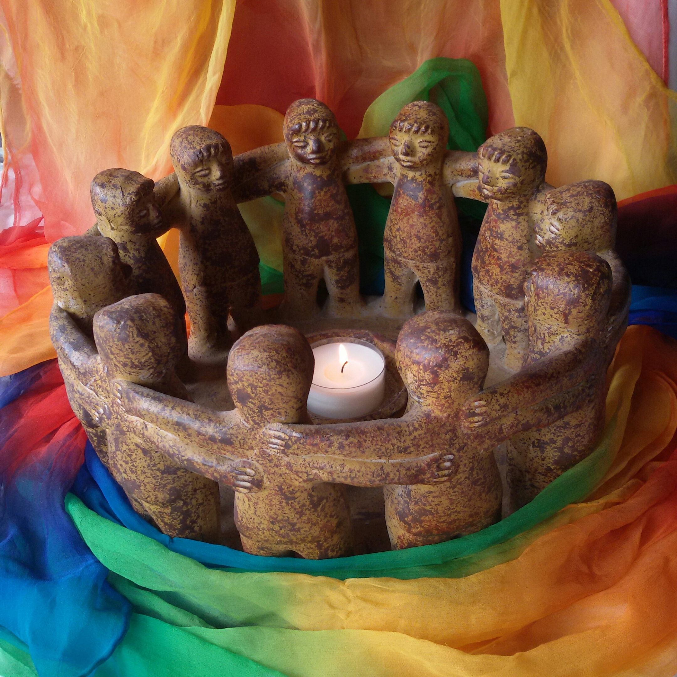 Zusehen ist eine Gruppe Figuren, die um ein Teelicht tanzen und von einem bunten Tuch eingerahmt ist.