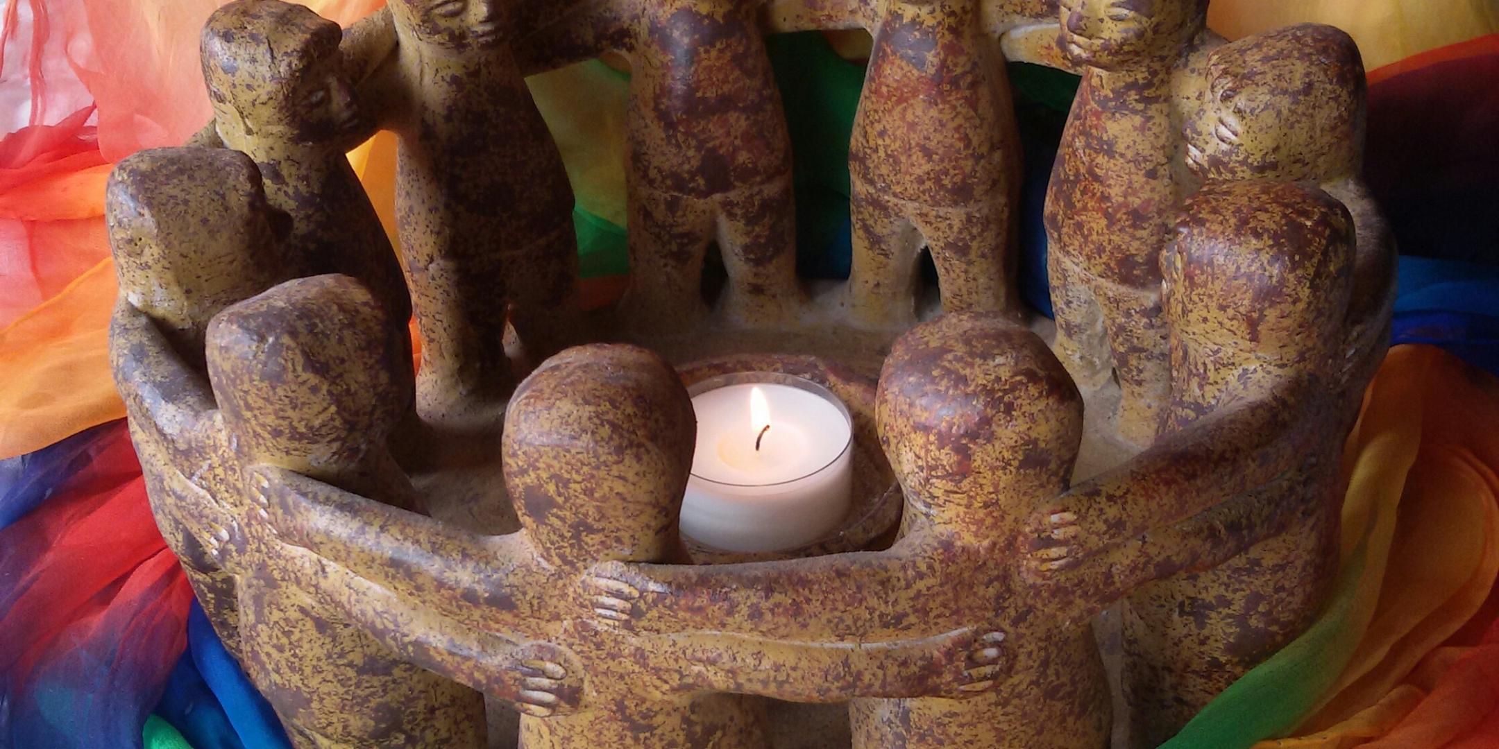 Zusehen ist eine Gruppe Figuren, die um ein Teelicht tanzen und von einem bunten Tuch eingerahmt ist.