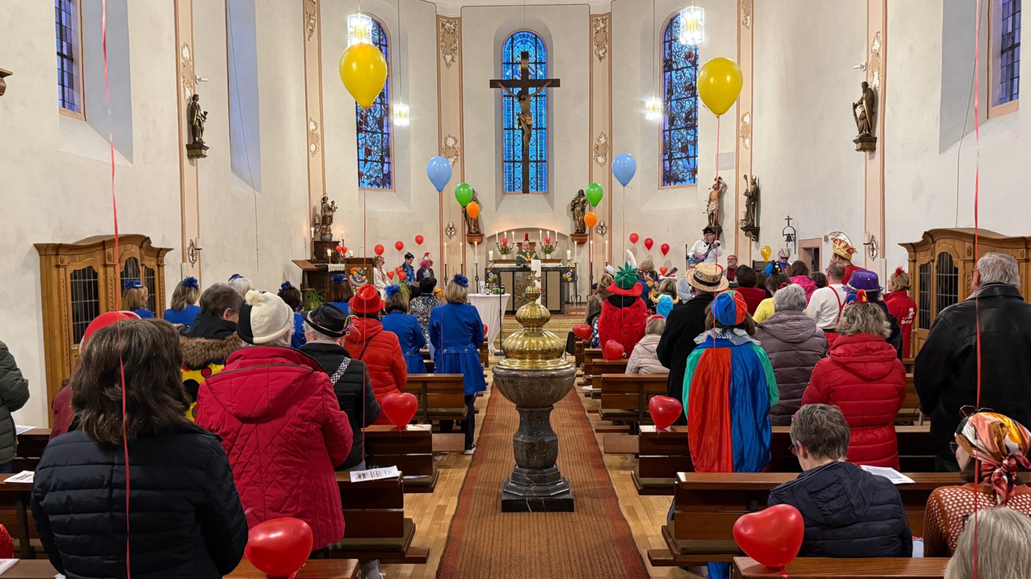 Zu sehen ist die Kirche in Burgen mit bunt kostümierten Besuchern und Luftballons als Dekoration