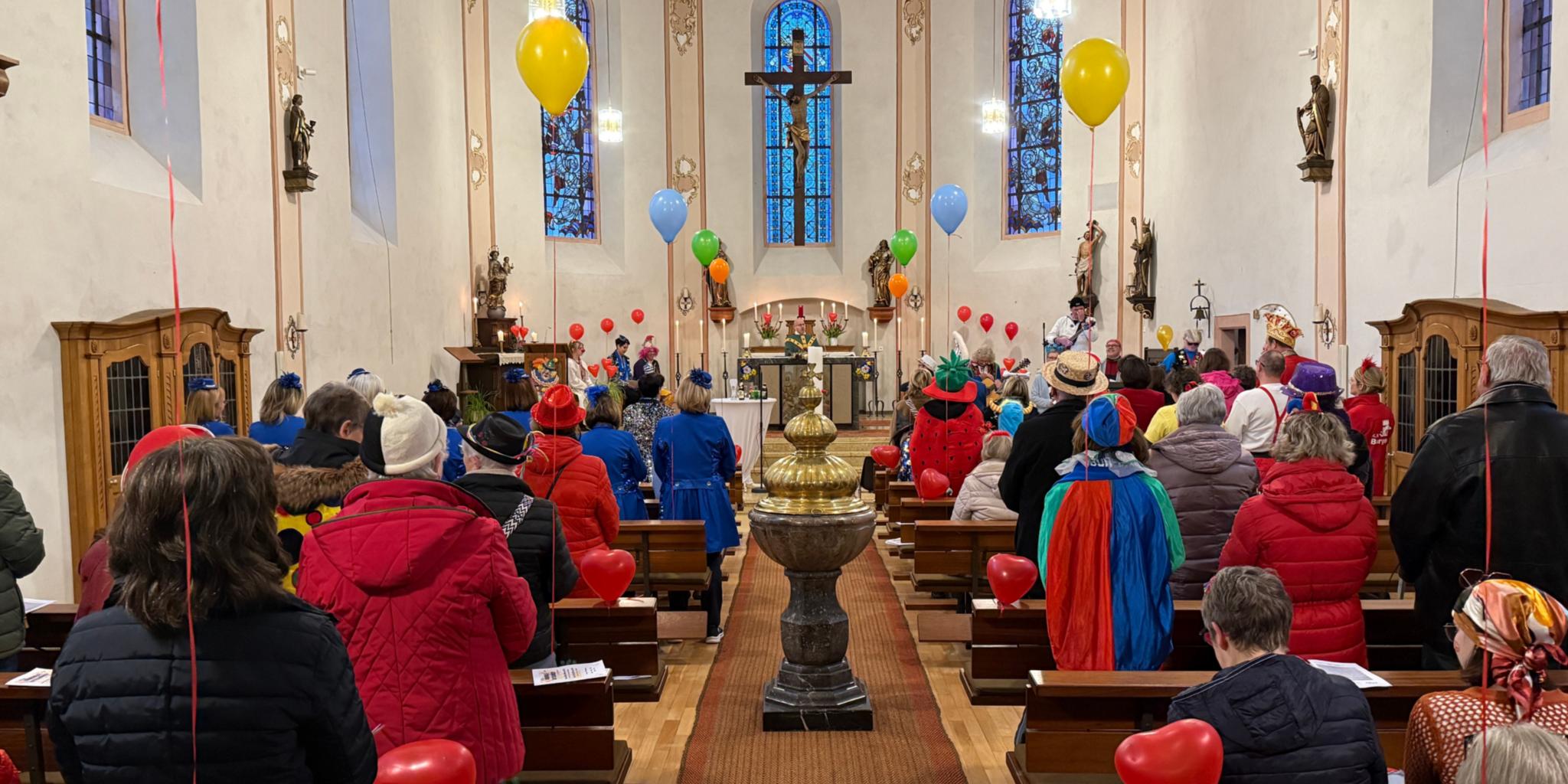 Zu sehen ist die Kirche in Burgen mit bunt kostümierten Besuchern und Luftballons als Dekoration