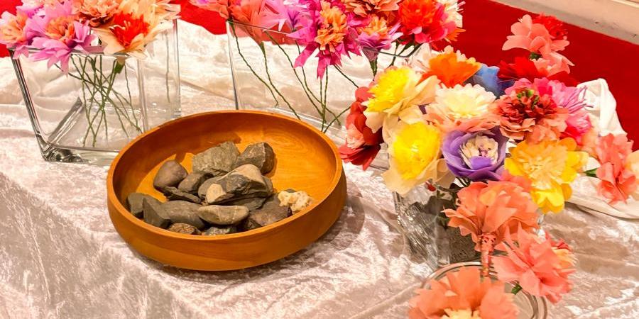 Auf einem Tuch vor dem Altar steht eine Keramikschale mit Steinen umringt von Vasen mit bunten Blumen.