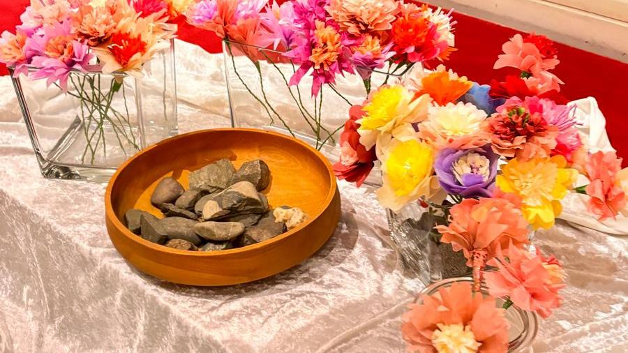 Auf einem Tuch vor dem Altar steht eine Keramikschale mit Steinen umringt von Vasen mit bunten Blumen.