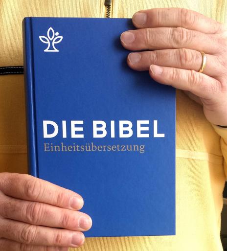 Zu sehen ist eine blaue Bibel, die von zwei Händen gehalten wird.